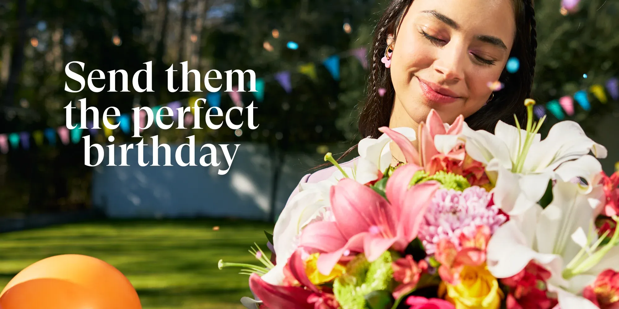 Banner Smiling woman holding a colorful bouquet in a garden with balloons and bunting, next to the text “Send them the perfect birthday” – Enviaflores.